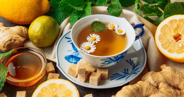 media-cup-chamomile-tea-with-lemons-ginger-brown-sugar-cubes-honey-glass-bowl-green-leaves-saucer-grey-piece-cloth-background-close-up