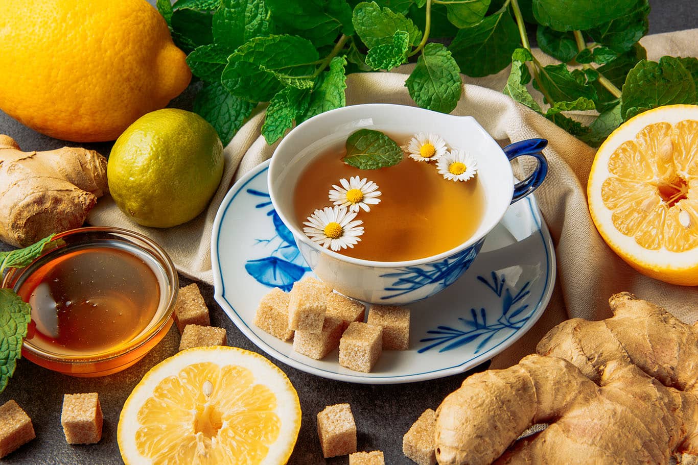 media-cup-chamomile-tea-with-lemons-ginger-brown-sugar-cubes-honey-glass-bowl-green-leaves-saucer-grey-piece-cloth-background-close-up